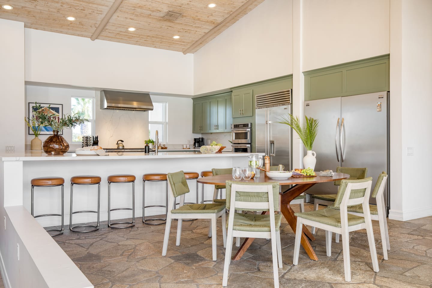Chef's kitchen with green cabinetry opening onto a long dining table
