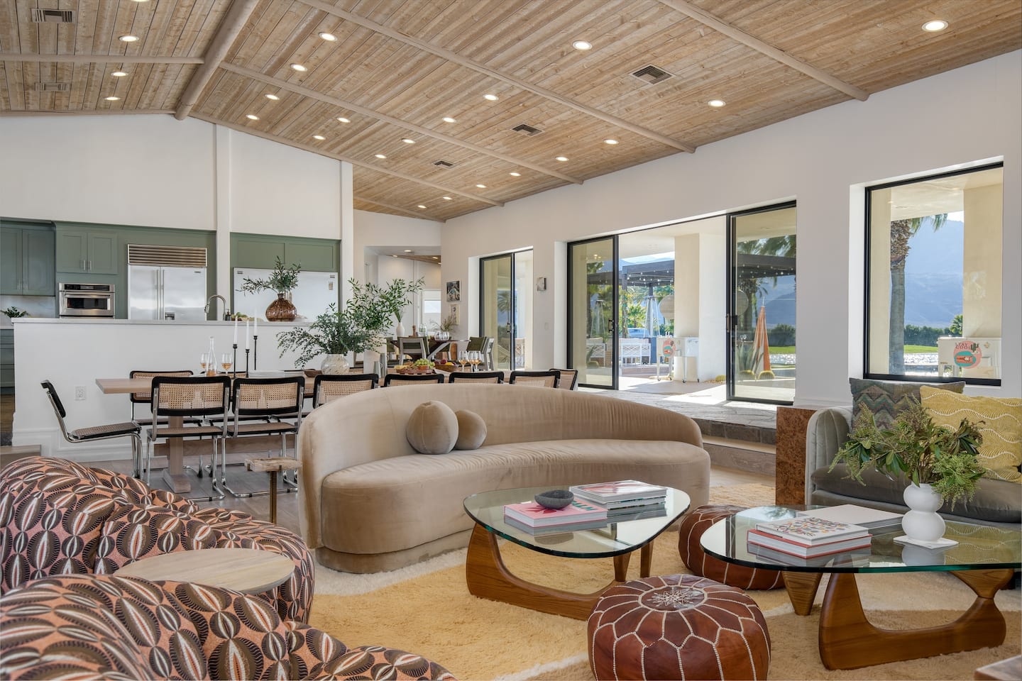 Open-plan living room with a curved sofa, vaulted wood ceiling, and pool views